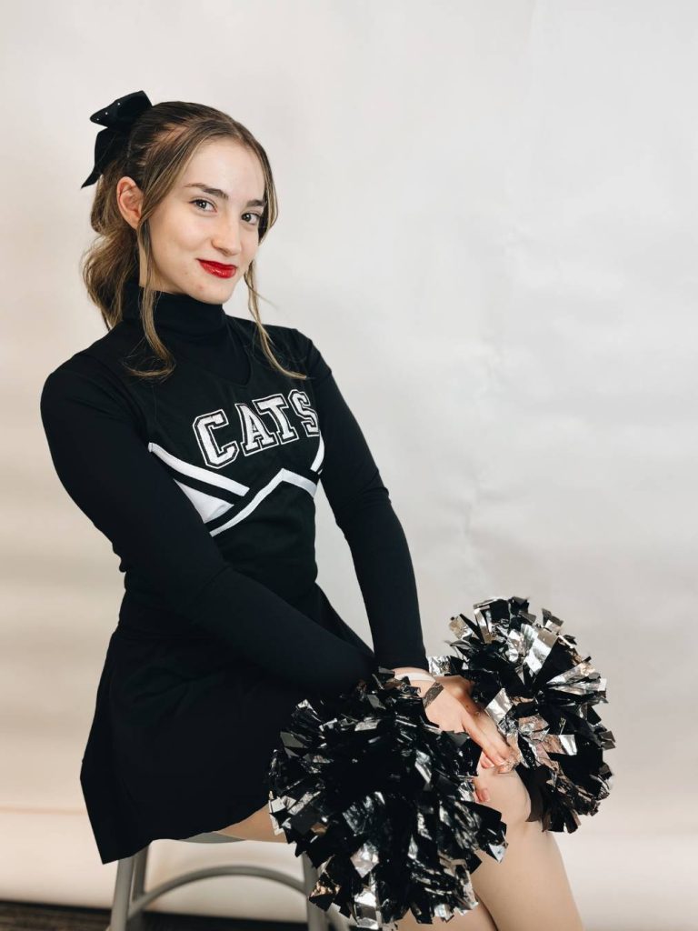 Female student in cheerleader uniform sitting in front of white screen